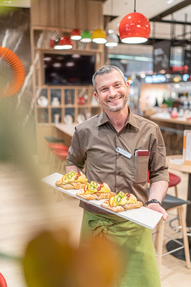 Wolfgang Garz, Leitung des Interspar Restaurant & Cafe Cappuccino in Villach, präsentiert drei frisch gebackene Obstplunder auf einer langen Servierplatte.