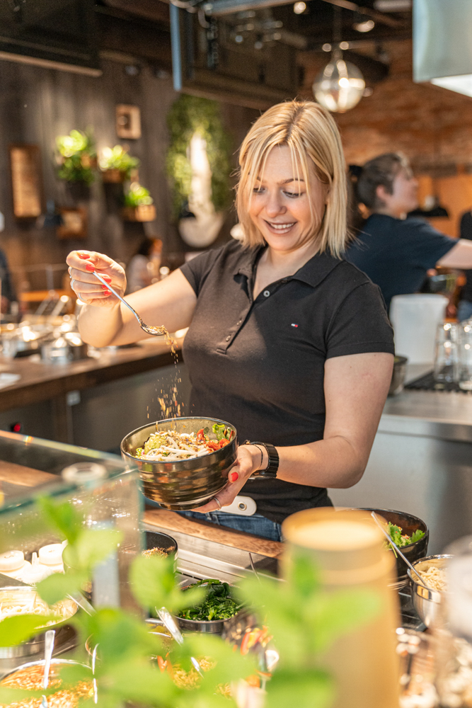 Mitarbeiterin richtet eine Bowl an und streut Zutaten darüber im My Indigo Restaurant, Atrio Villach.