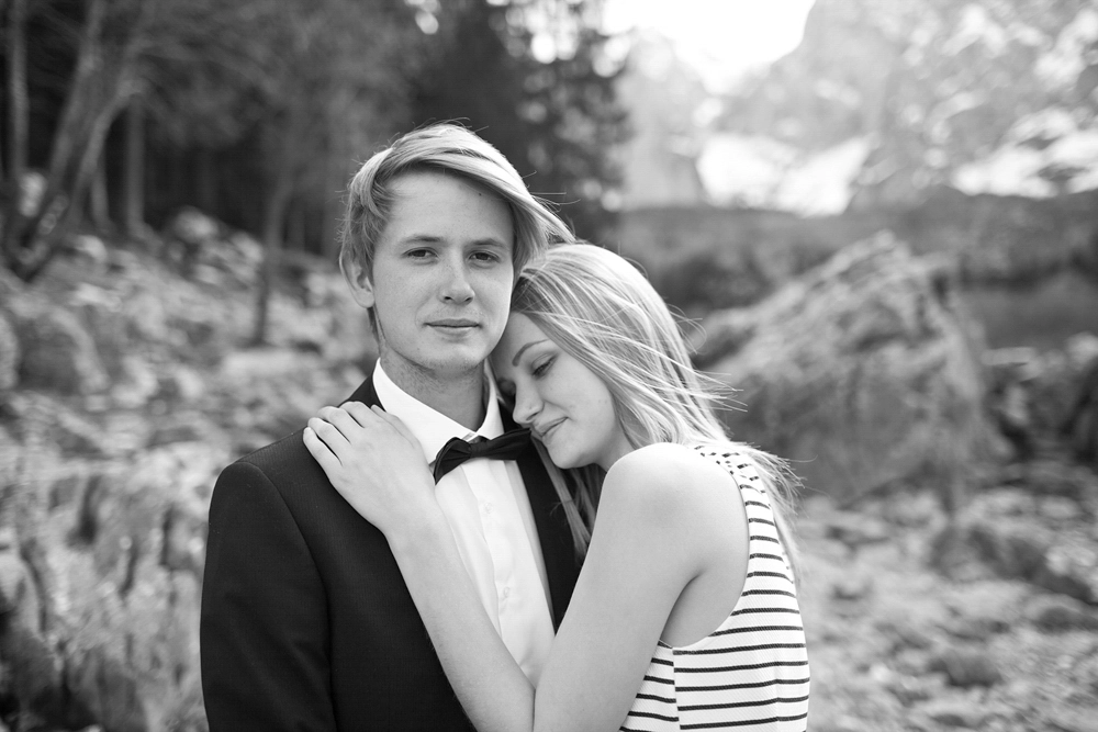 Junger Mann im Anzug, Frau lehnt sich an seine Schulter, emotionales Paarfoto am See in Kärnten