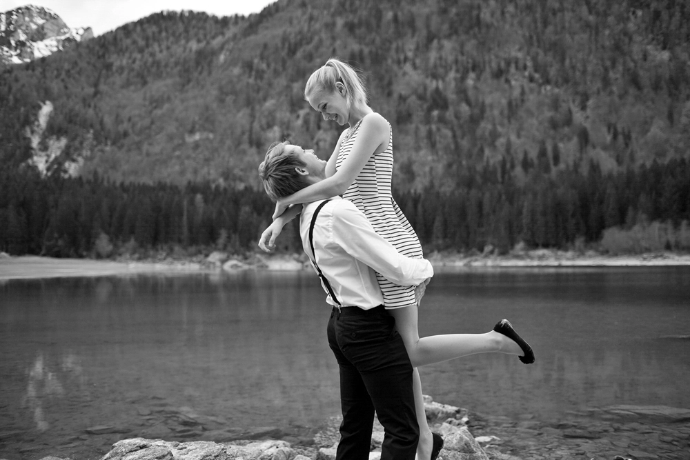 Mann hebt seine Partnerin lachend hoch am Seeufer, emotionale Paarfotos in Kärnten nahe Villach